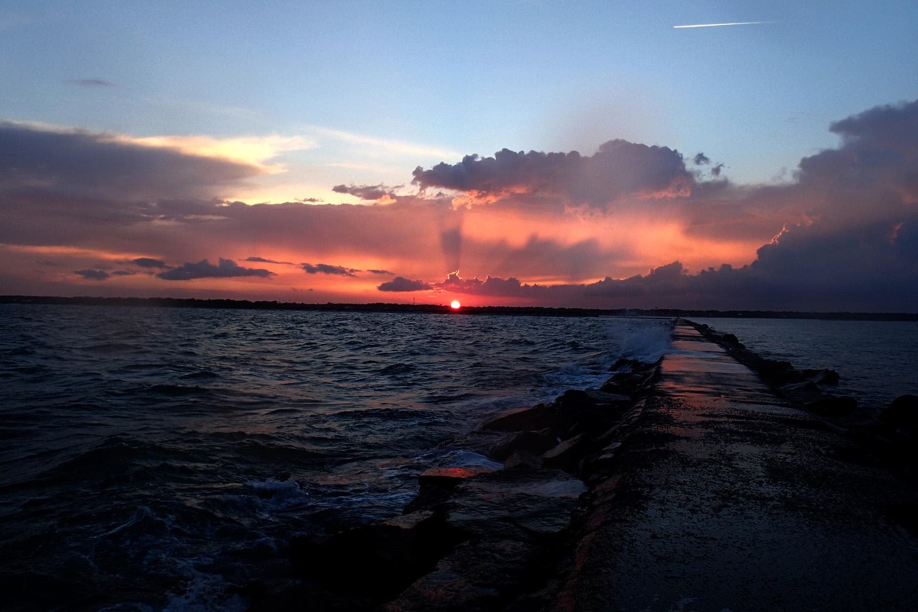 Orange sunset over ocean jetty, scenic coastal paddling view