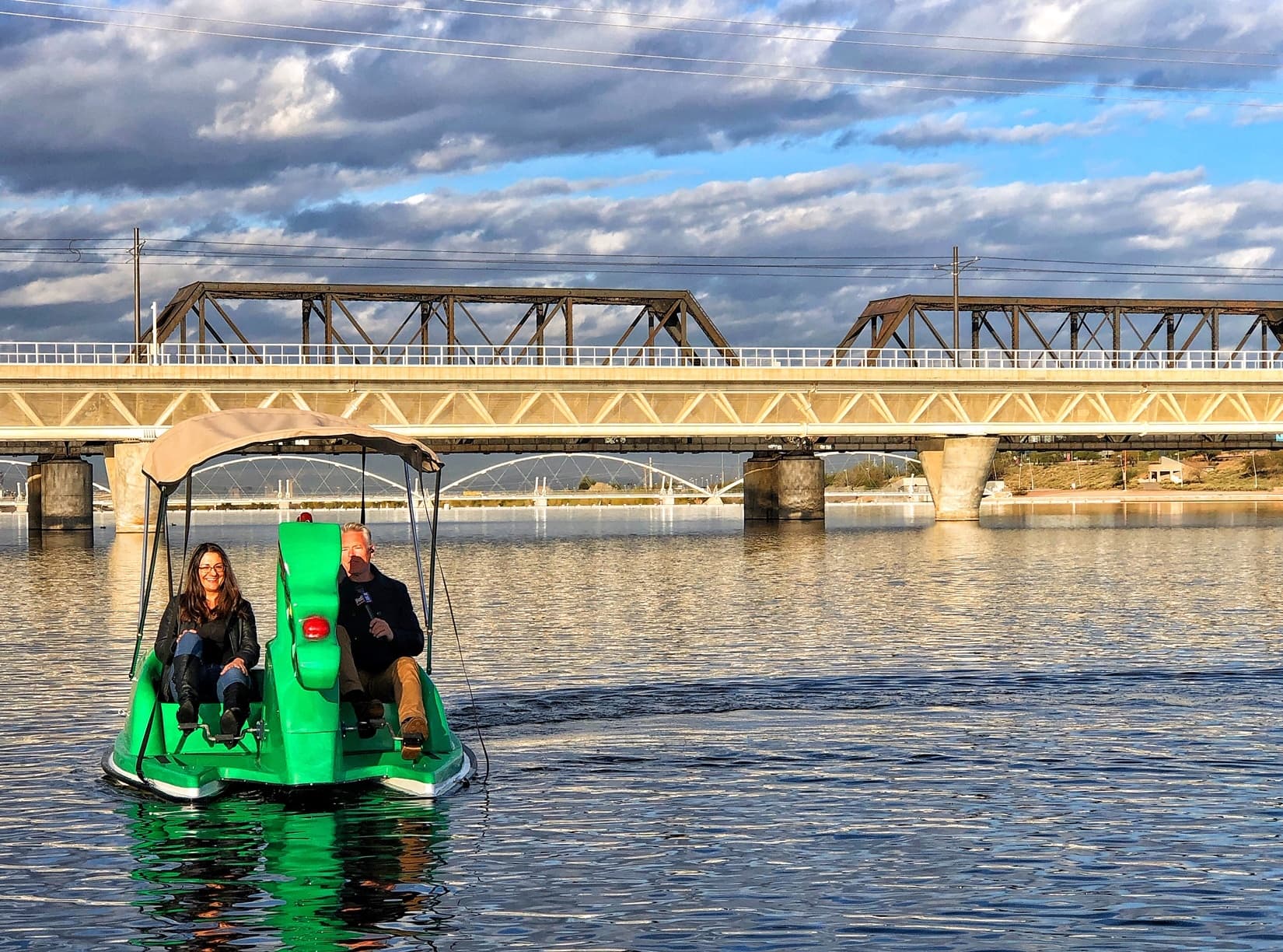 Two riders on green paddleboat under bridge on Kiwanis Lake