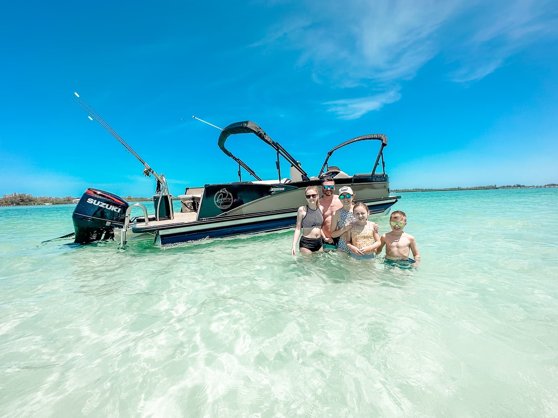 Family swimming beside anchored boat in clear shallow turquoise water