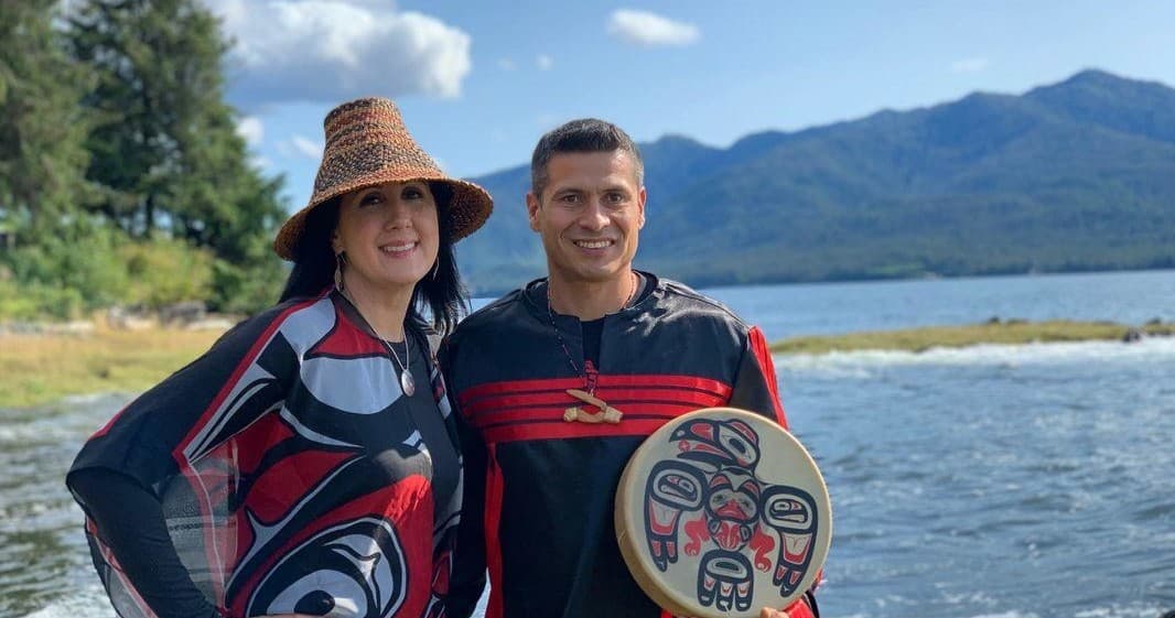Native performers in regalia on lake shore with Alaskan mountains
