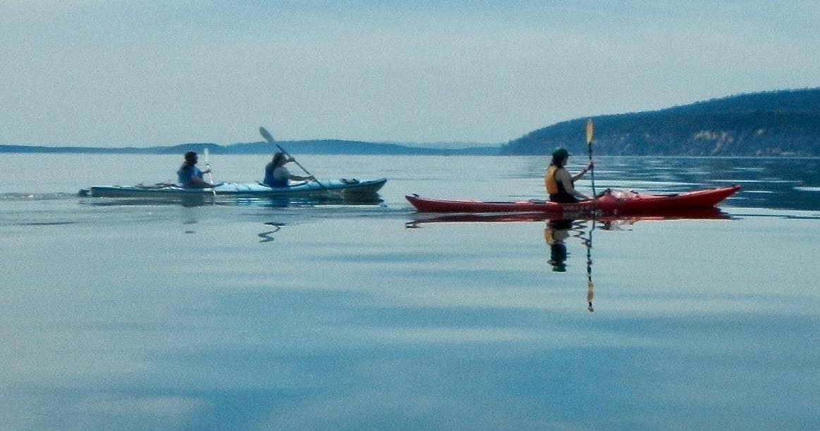 Three kayakers paddling on calm coastal waters at sunrise