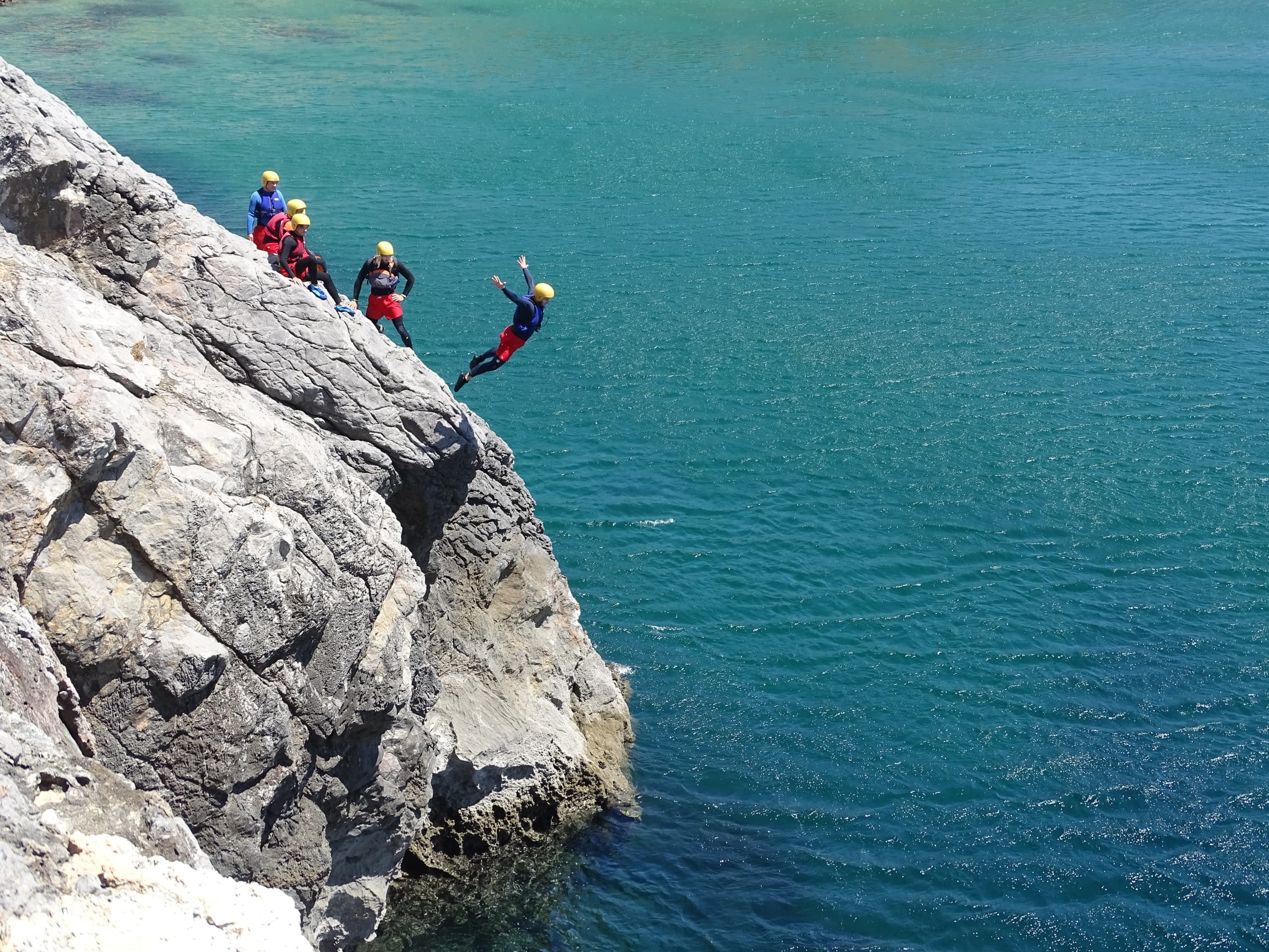 Cliff jumpers leaping into blue ocean from rocky Algarve headland