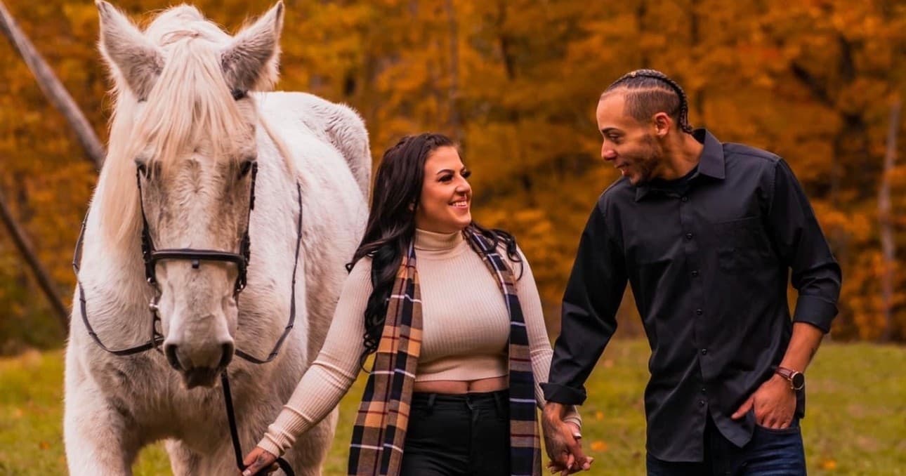 Couple walking beside white horse in autumn woods
