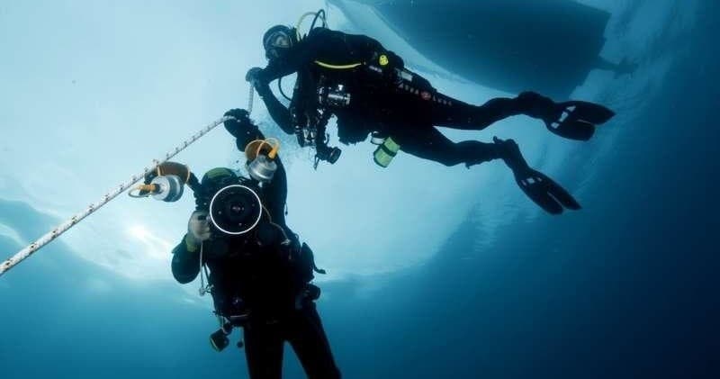 Two scuba divers ascending toward surface beside anchored dive boat