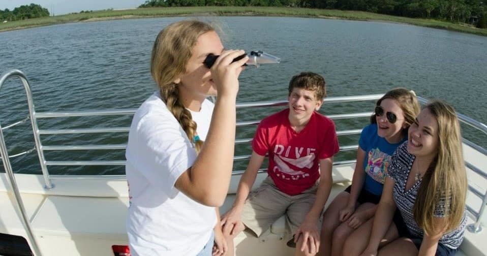 Teen using binoculars on boat overlooking coastal marsh wildlife