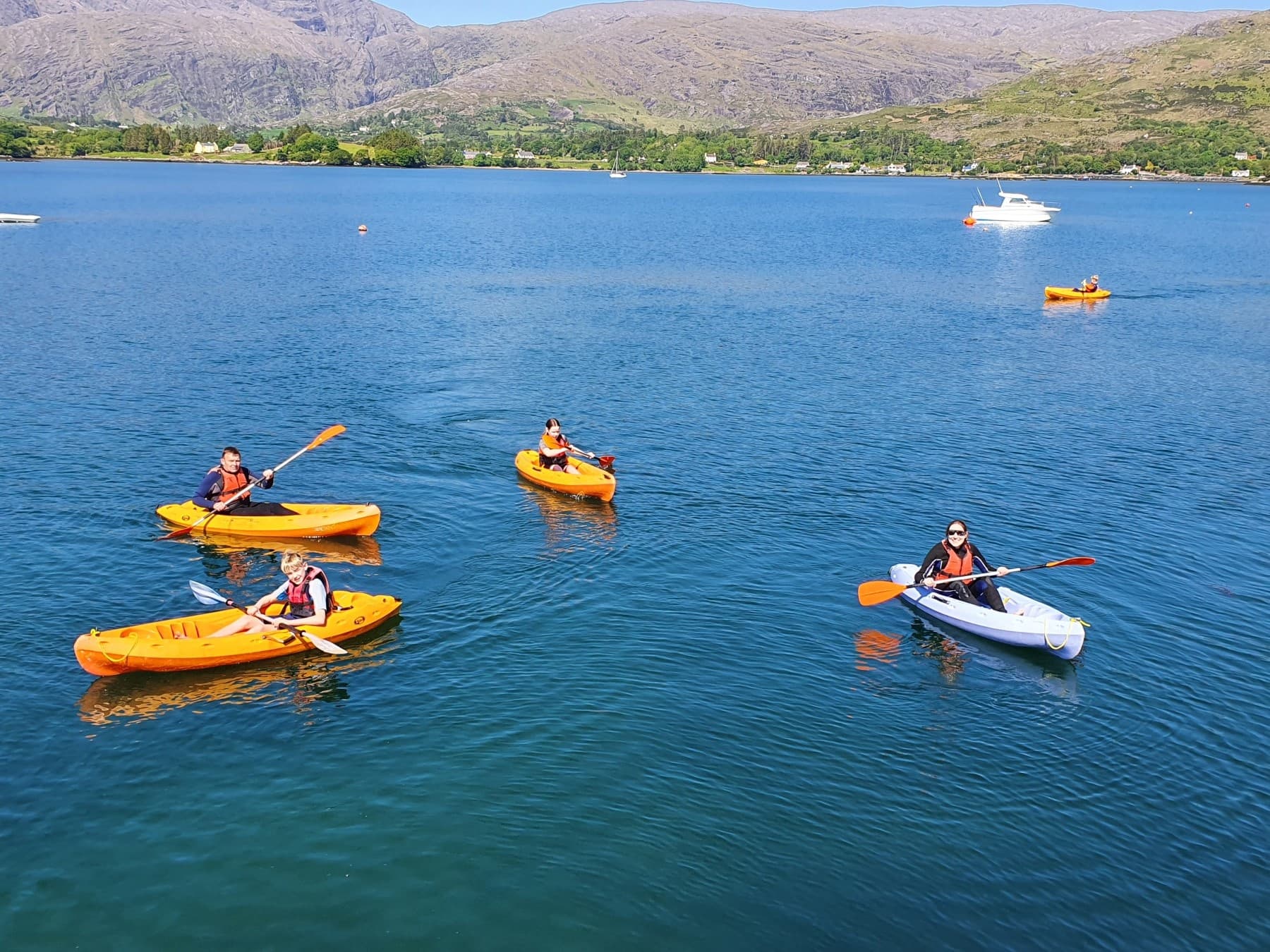 Kayakers paddling in a calm coastal bay with mountain backdrop