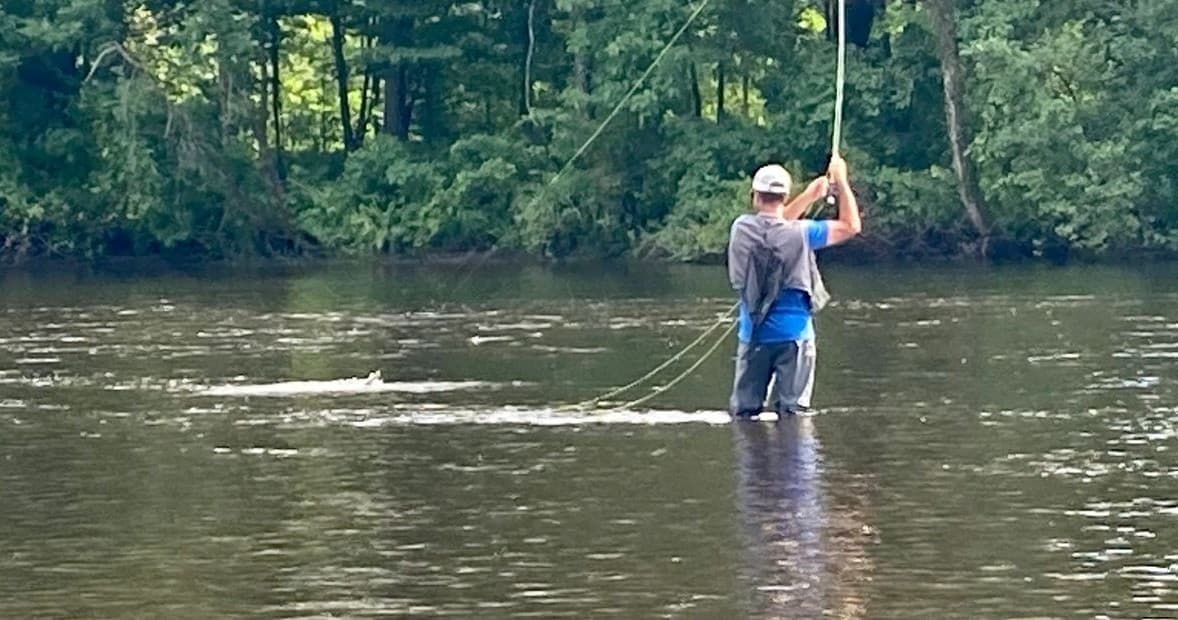 Angler fly fishing waist-deep in forested river current