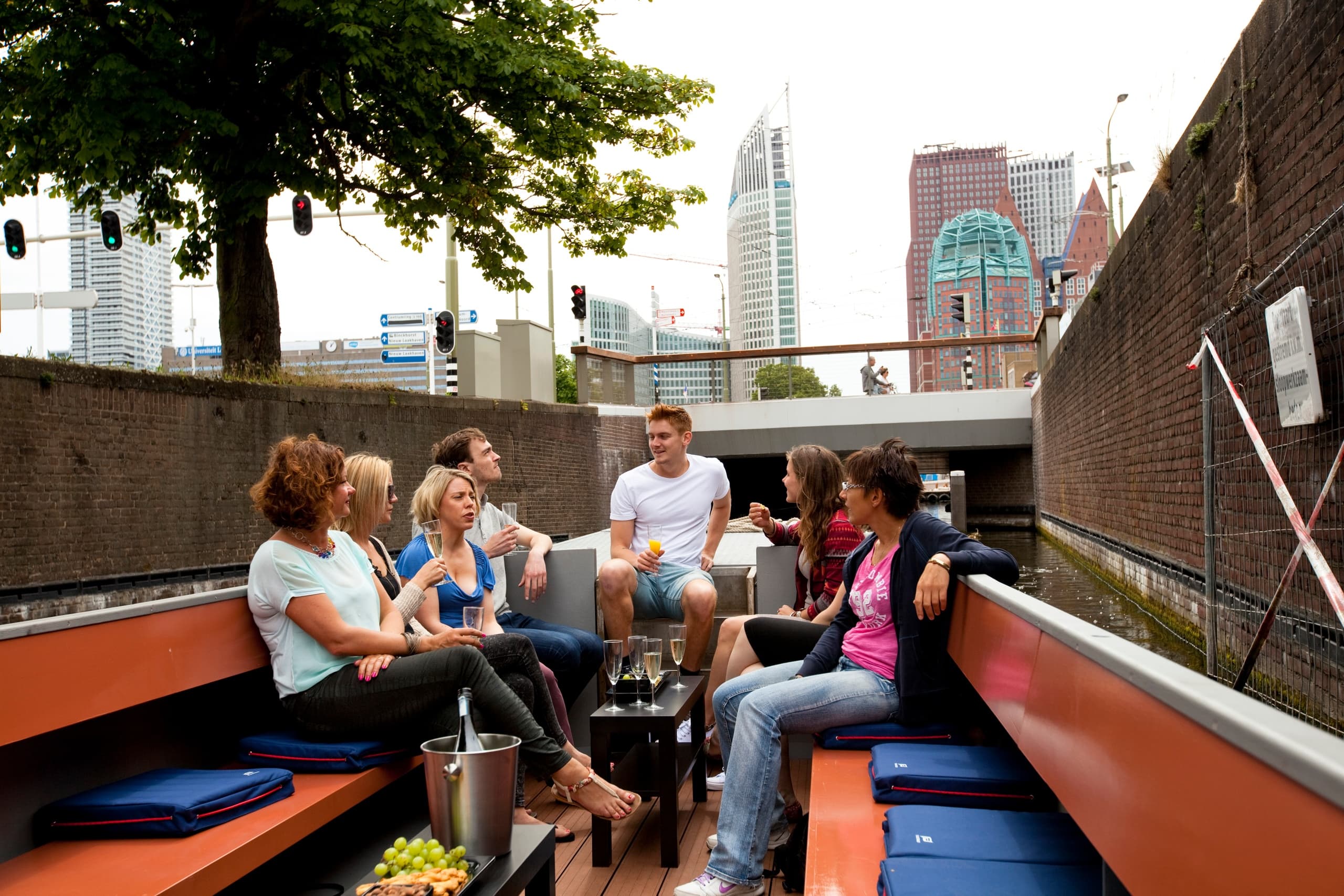 Small group socializing on open canal boat with city skyline backdrop
