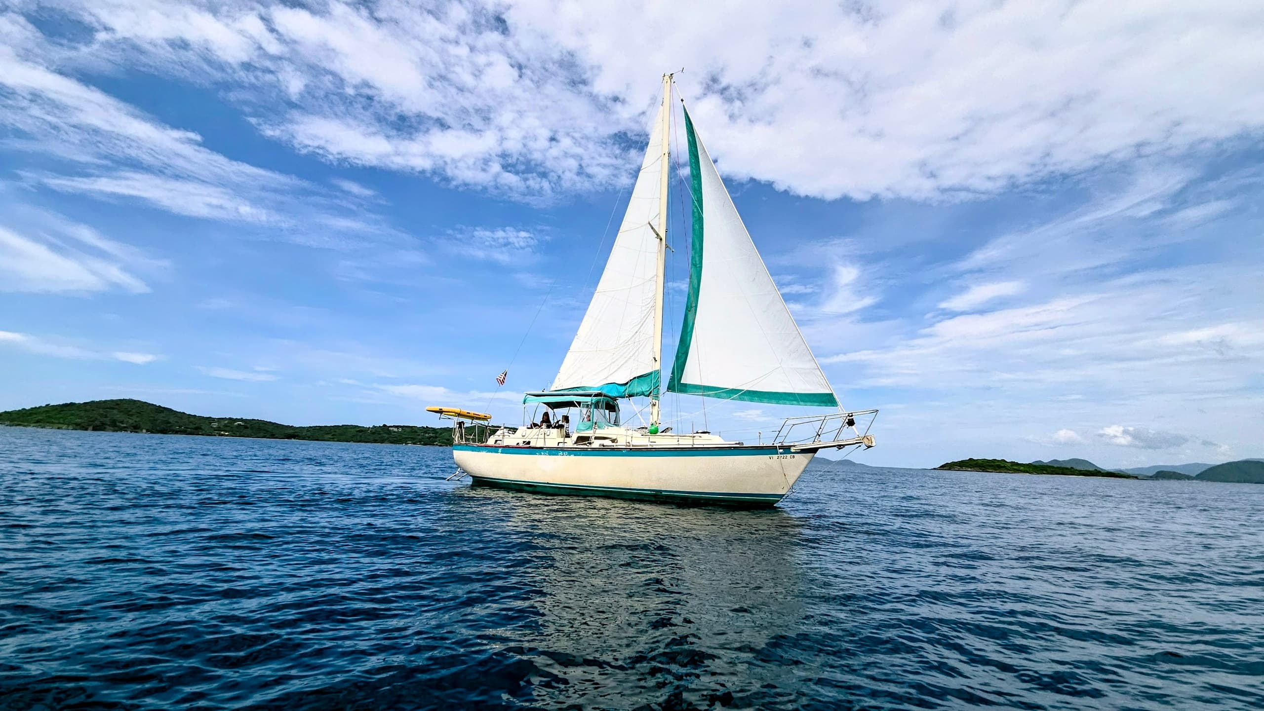 Sailboat cruising on clear ocean with dramatic sky and islands