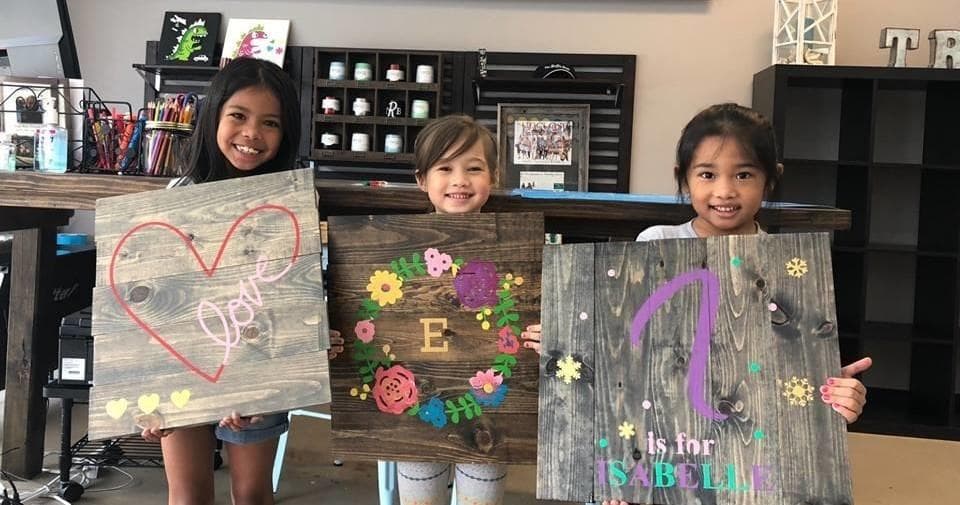 Children showing painted wooden signs in indoor art workshop