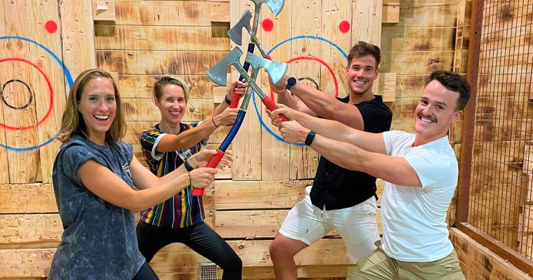 Friends cheering while holding axes at indoor target lanes celebrating