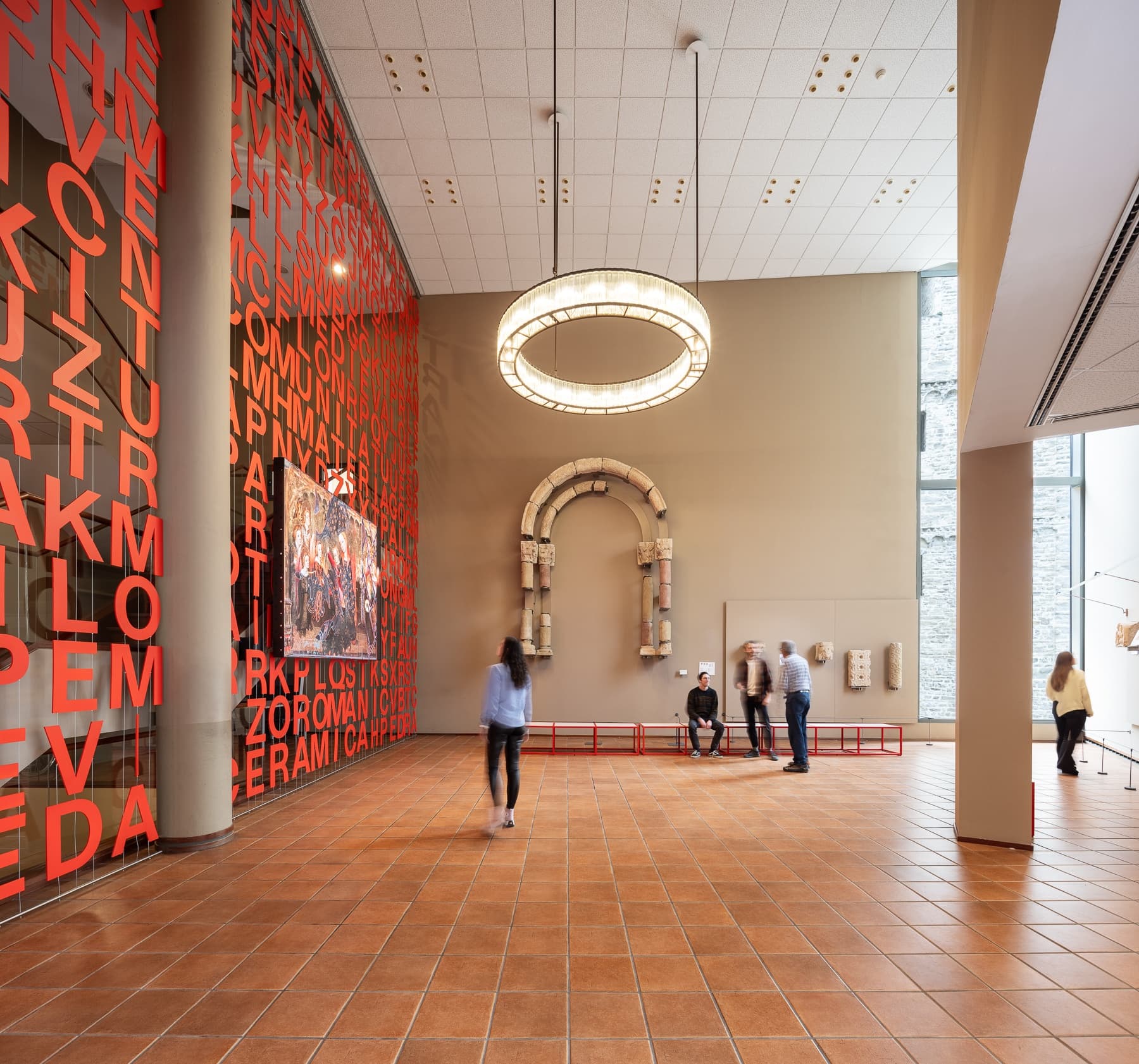 Visitors walking through spacious museum atrium with large red mural