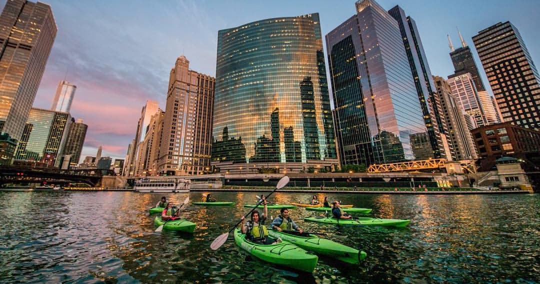 Kayakers paddling at sunset with city skyline reflection on water