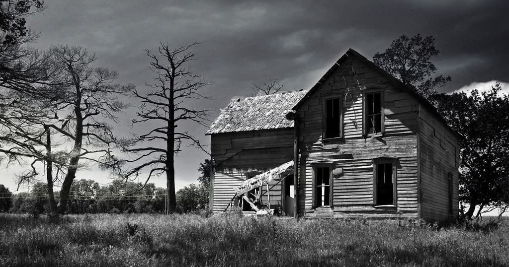Dilapidated farmhouse in rural field under moody sky