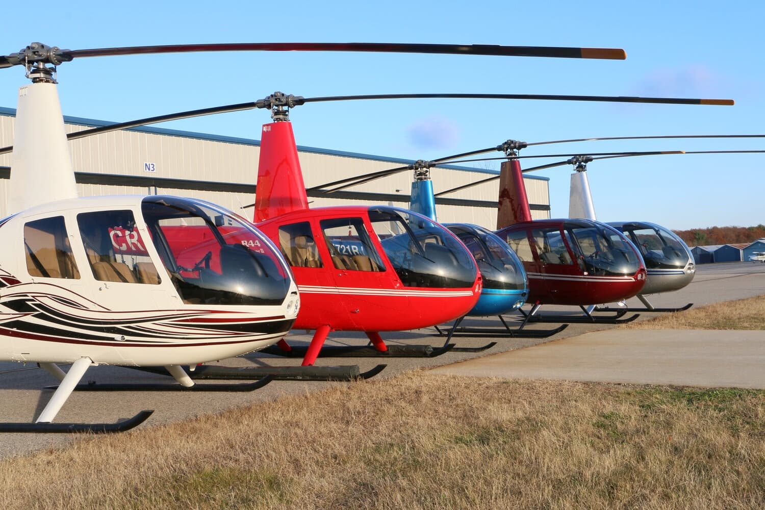 Helicopter tour fleet lined up on tarmac at grassy airfield