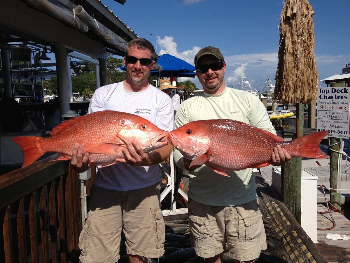 Two anglers holding large red snapper on dock after charter