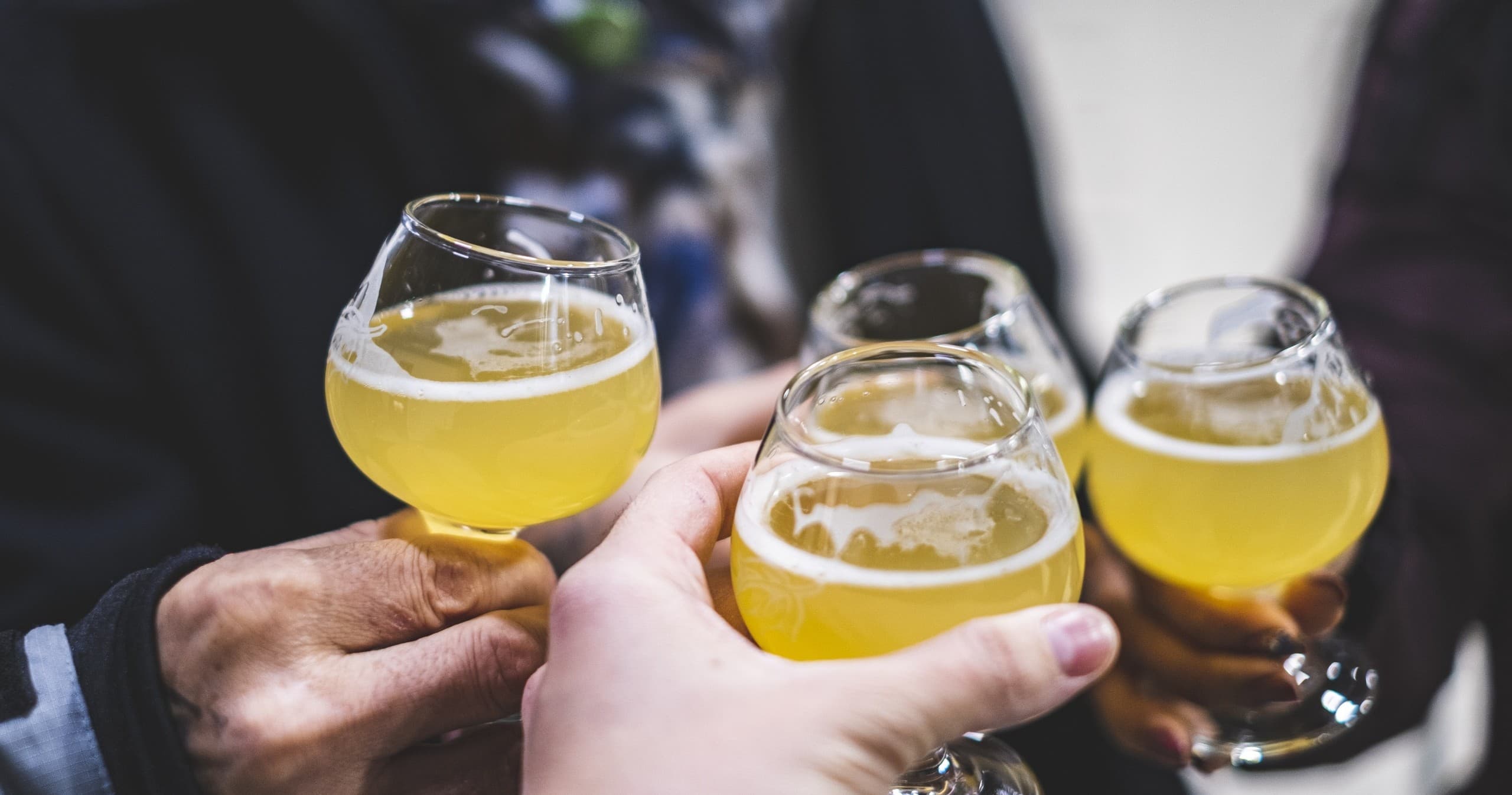 Friends clinking craft beer glasses outdoors on casual food tour
