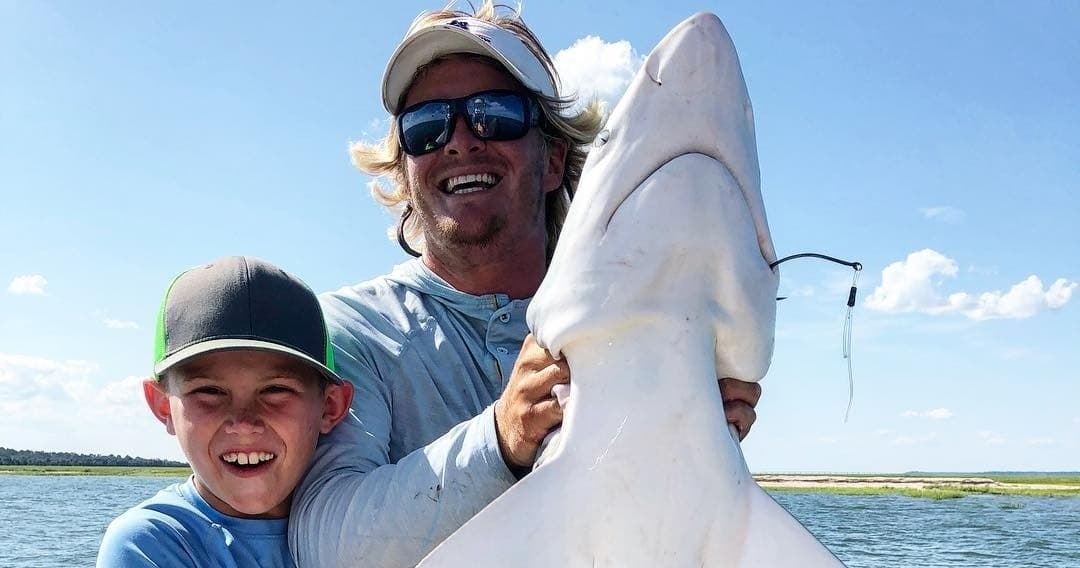 Father and son holding a large shark on coastal saltwater fishing charter