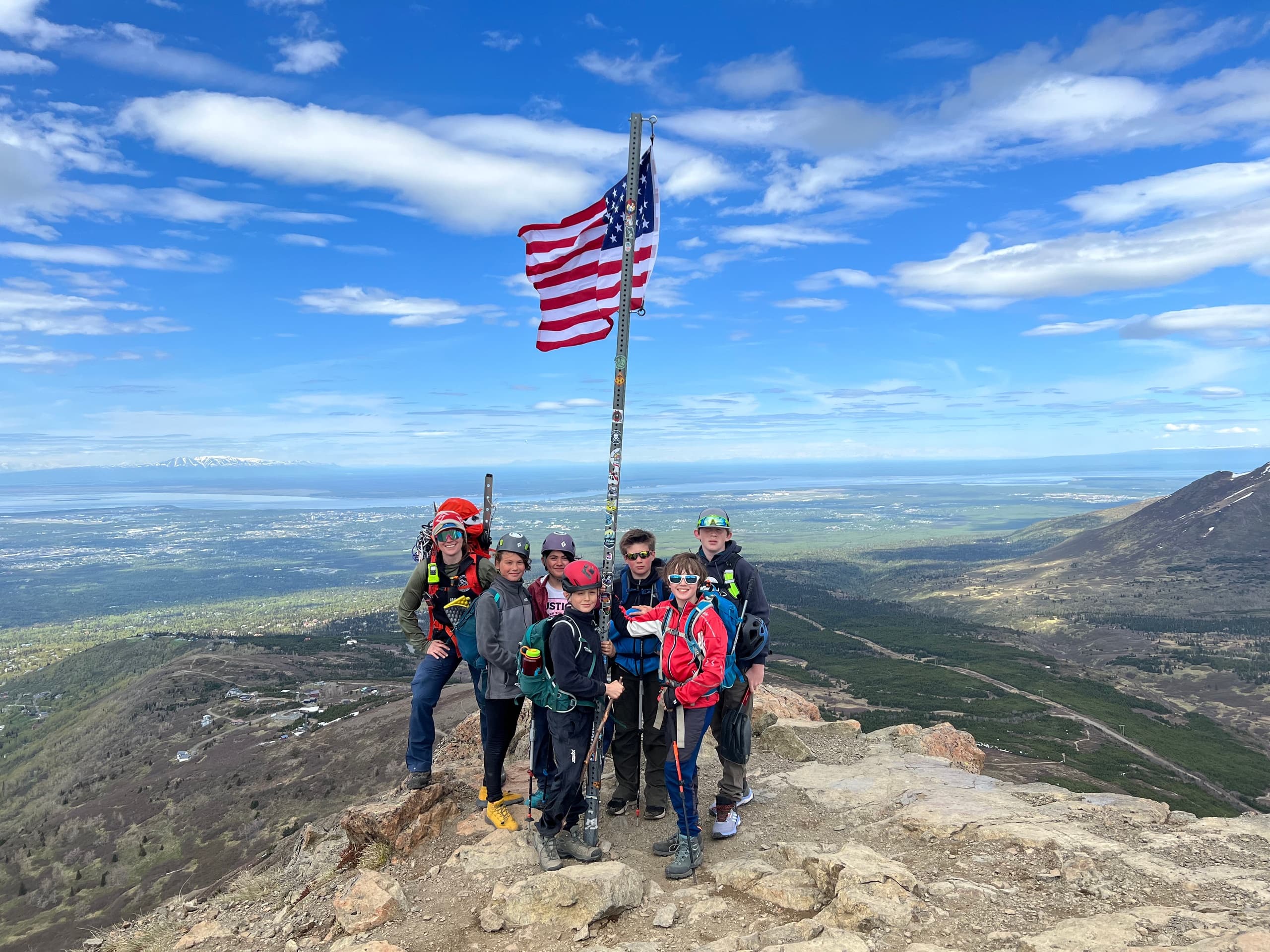 Summit hikers posing with American flag on alpine mountain ridge
