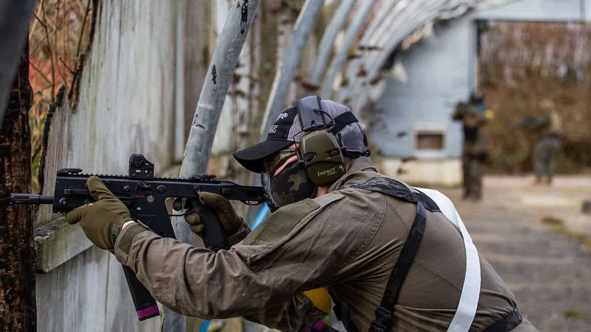 Airsoft player aiming rifle from outdoor cover in tactical field
