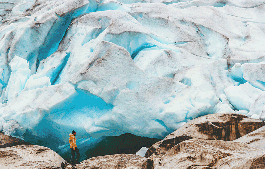 Hiker exploring vibrant blue glacier ice cave and rocky moraine