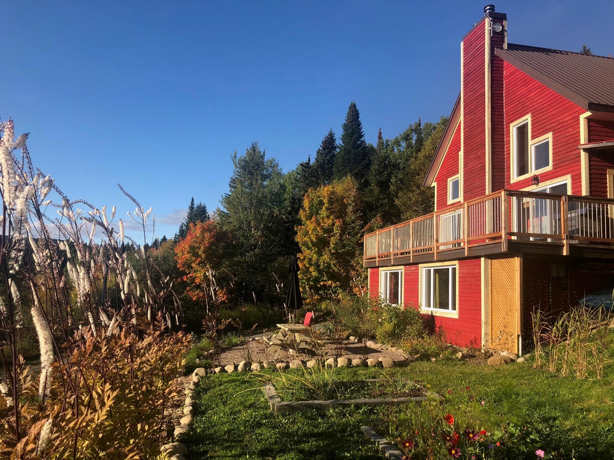Red mountain gîte exterior on hillside surrounded by autumn trees