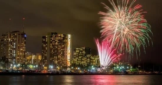 Fireworks over city skyline reflected on harbor at night