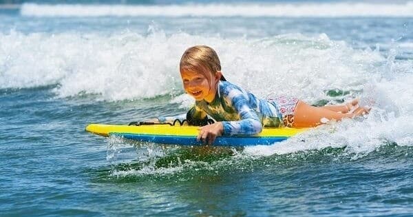 Child bodyboarding on breaking ocean waves at sunny beach