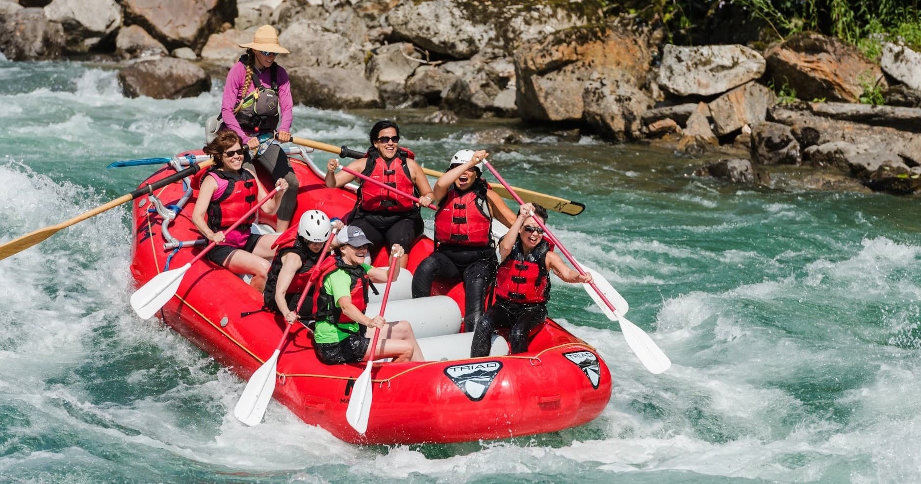 Guided whitewater rafting group paddling through rocky river rapids