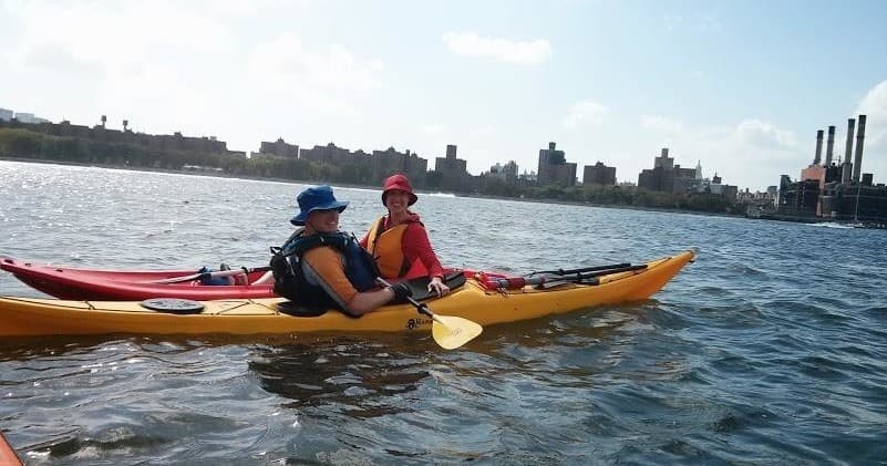 Tandem kayakers paddling along Brooklyn waterfront cityscape