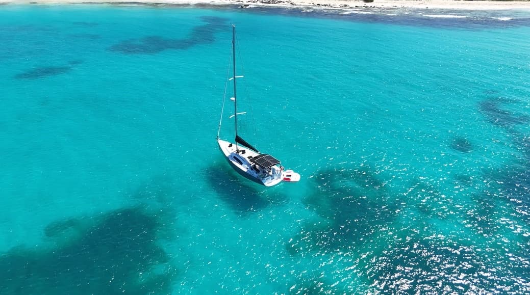 Aerial sailboat drifting in turquoise tropical ocean near shore