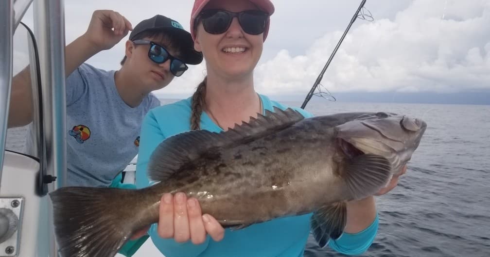 Smiling angler holding large grouper on offshore fishing charter