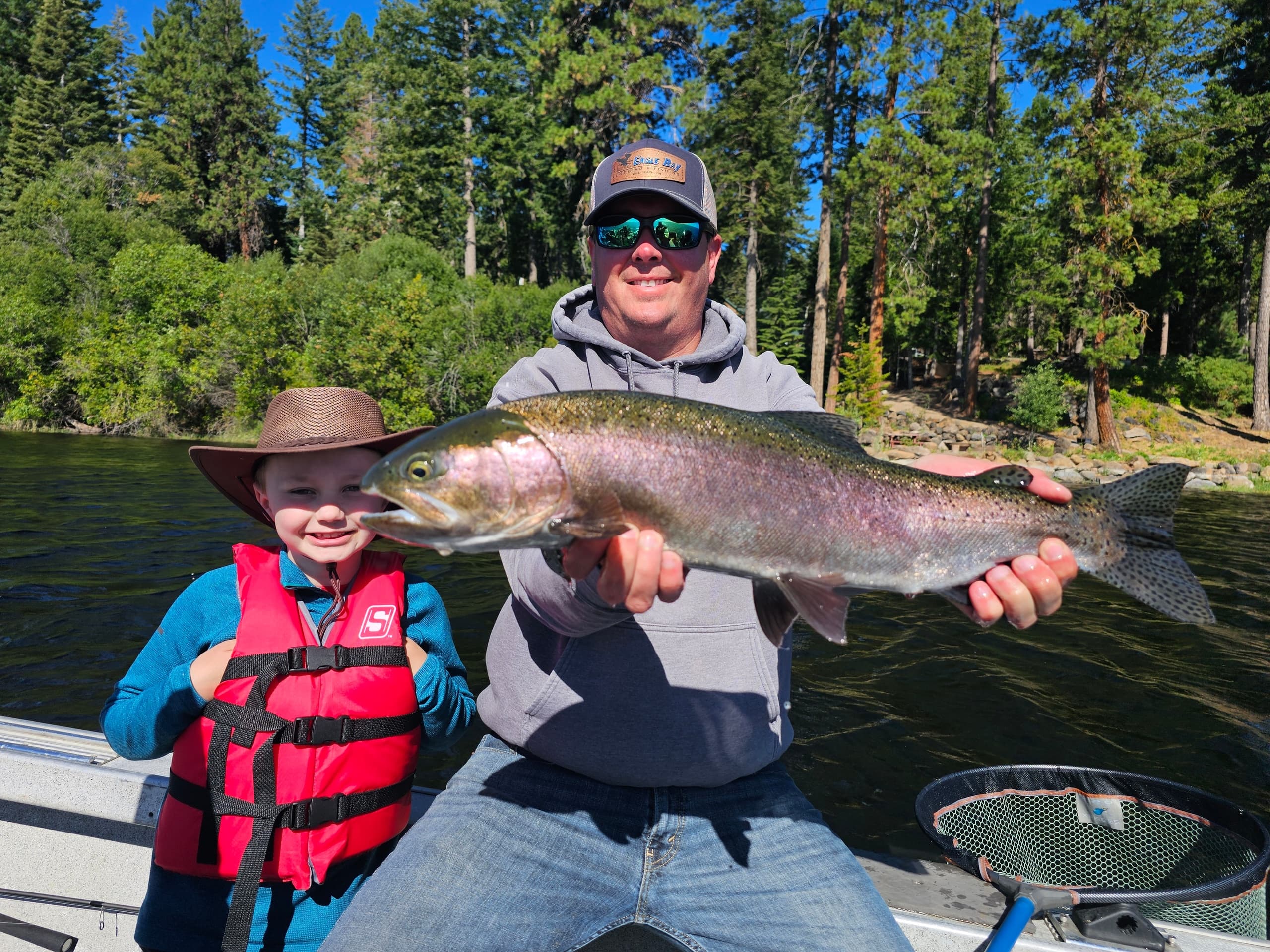 Father and child holding rainbow trout on river boat