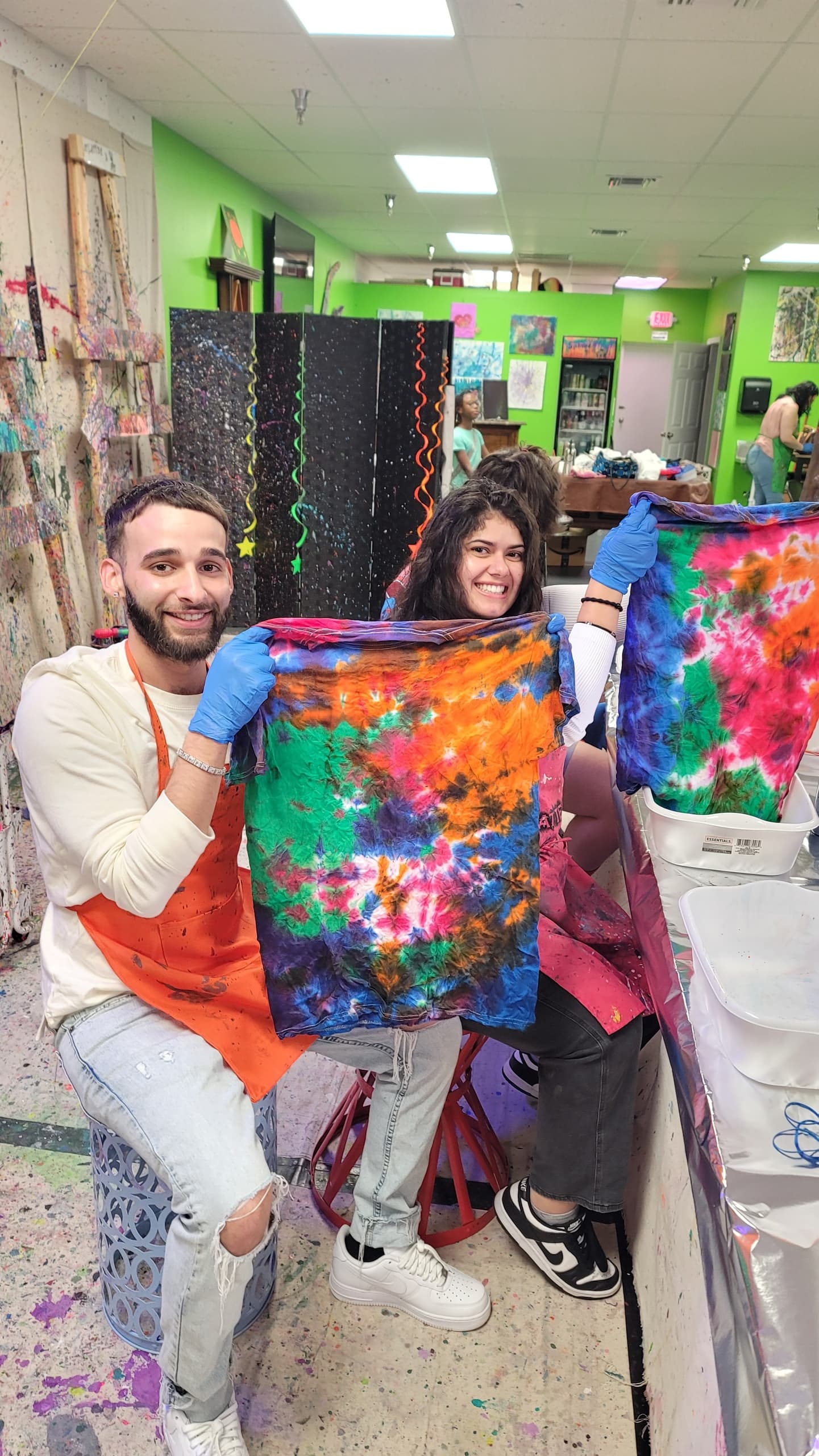 Couple holding vibrant tie-dye canvas in colorful indoor studio