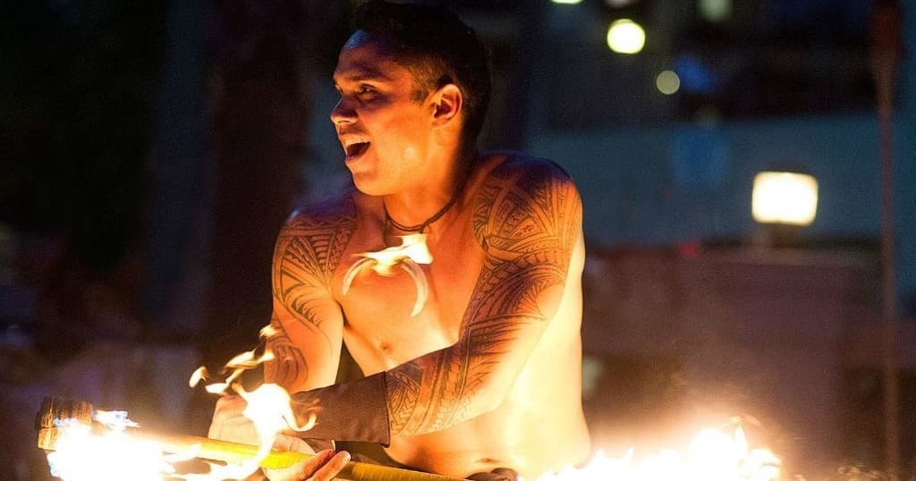 Polynesian performer spinning torches in dramatic night setting