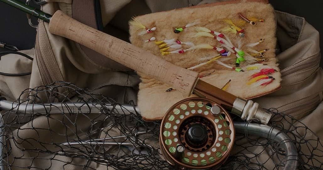 Fly fishing gear and flies staged on backpack by riverbank