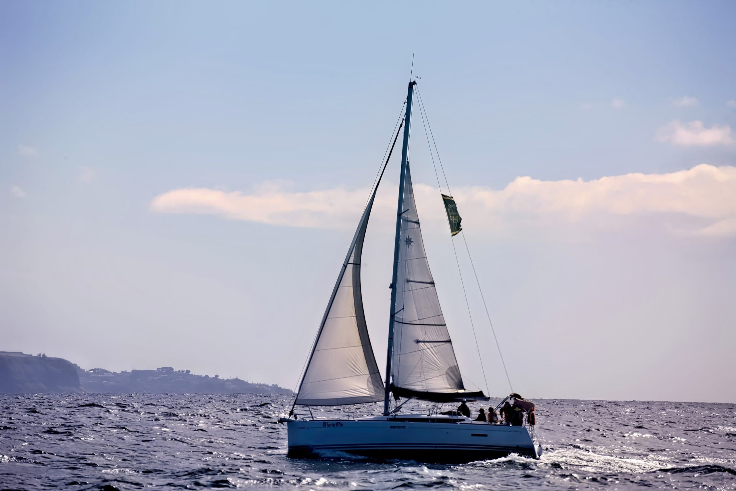 Sailboat under full sails on open sea with distant shoreline view
