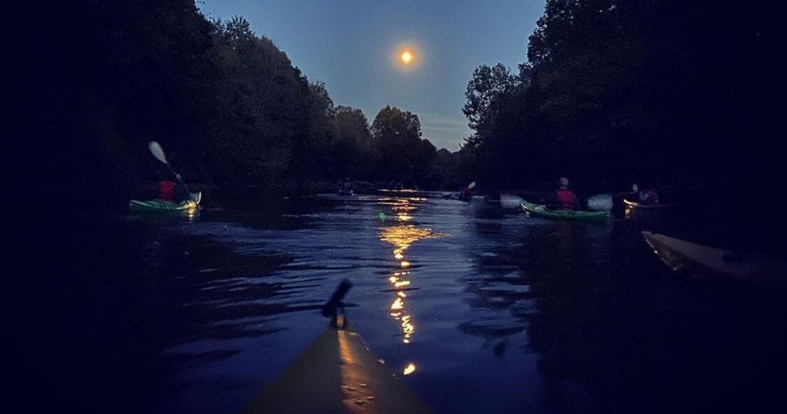 Night paddling under moonlight on tranquil river with kayaks