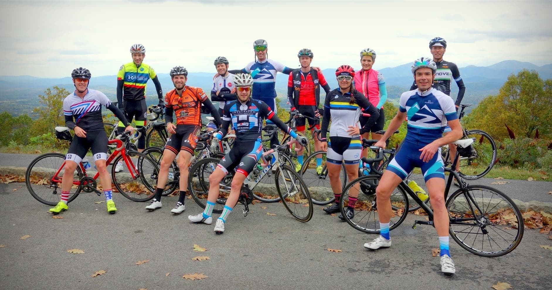 Group of road cyclists posing with bikes on scenic roadside ride