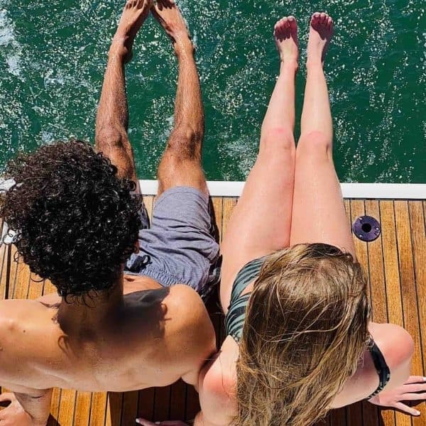 Two people relaxing on yacht swim platform, feet over green water