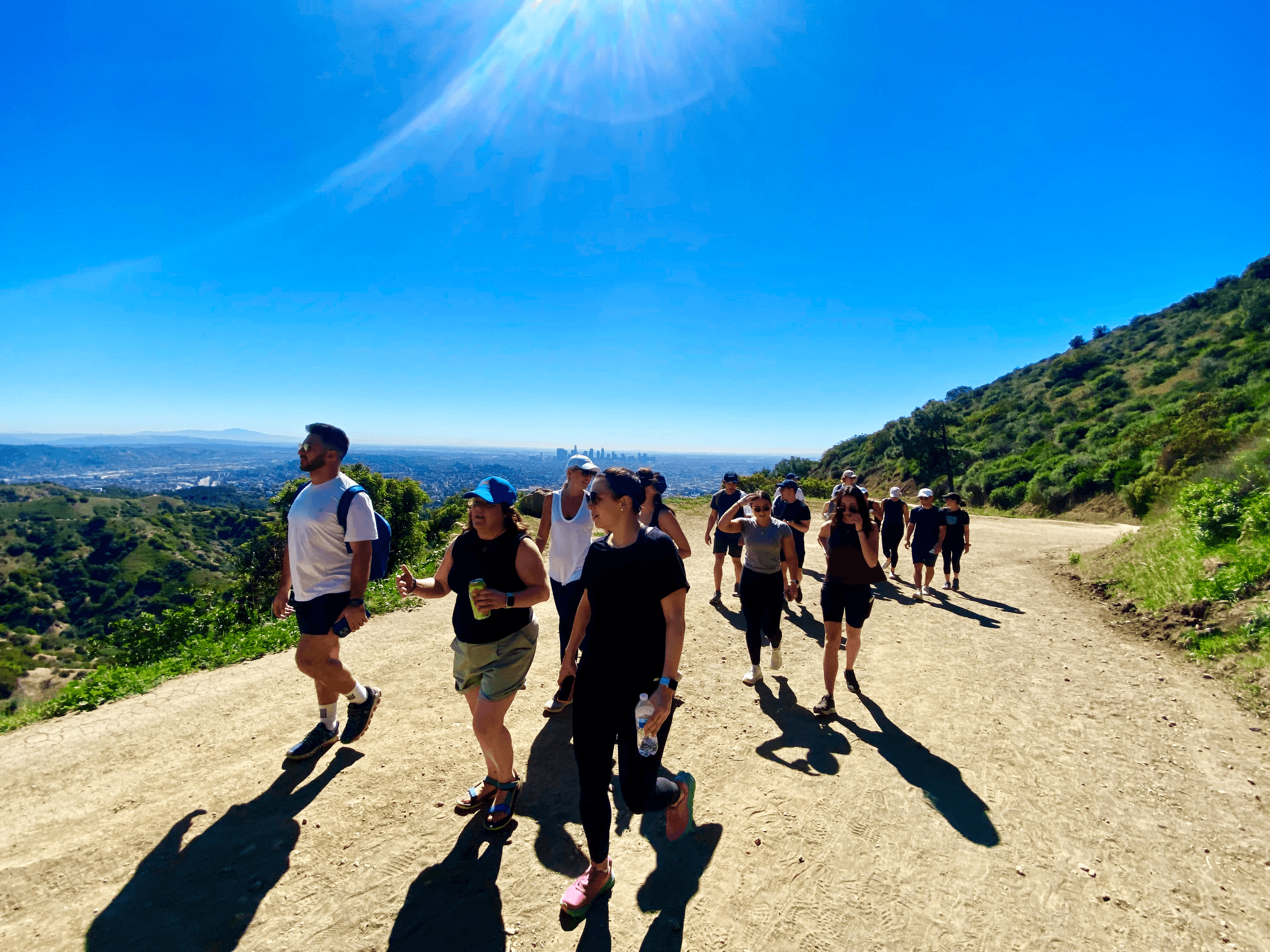 Group hiking along sunlit LA trail with coastal hills vista