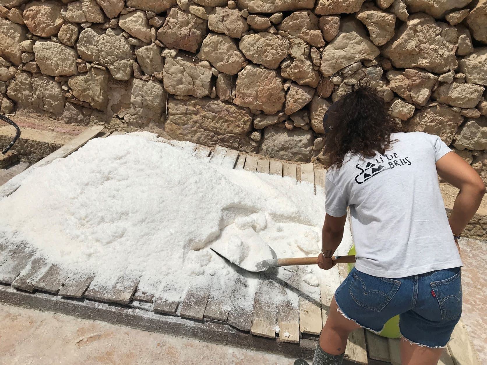 Worker shoveling harvested sea salt on coastal salt flats