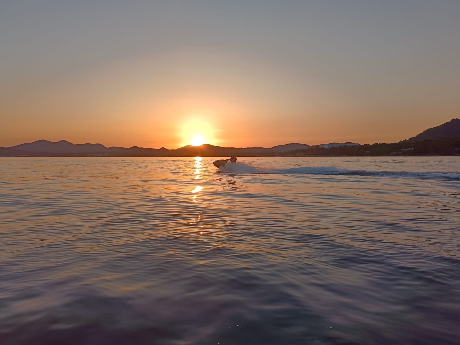 Sunset over calm sea with lone boat on horizon at coastal bay