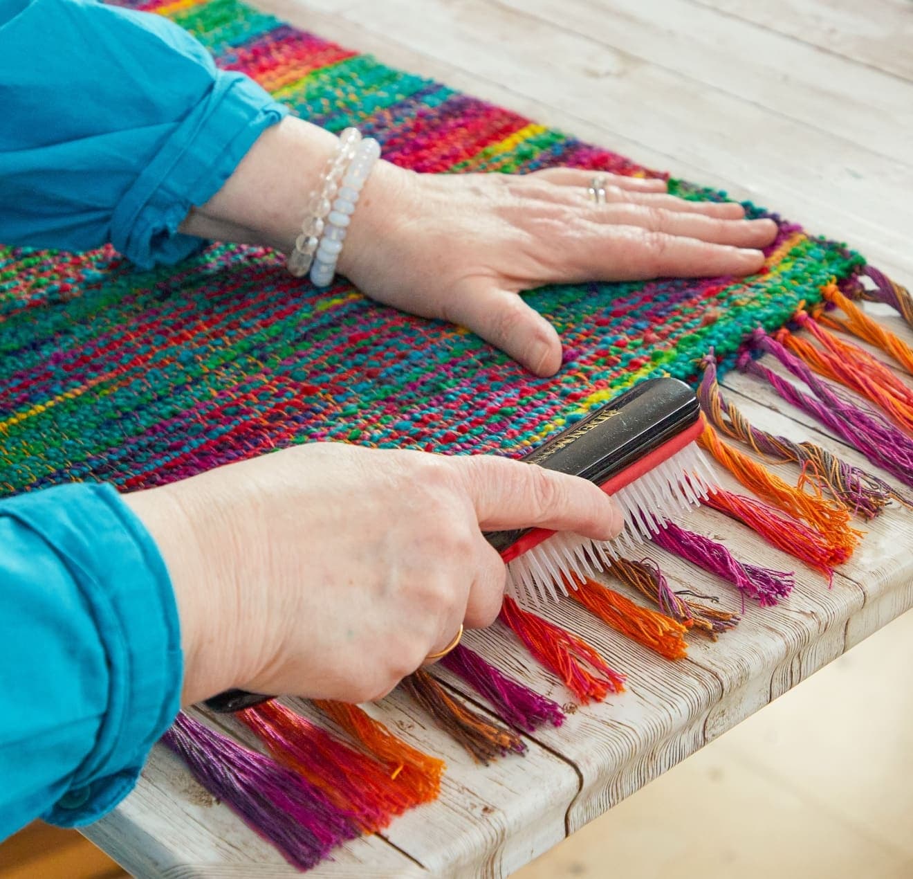 Hands brushing colorful woven textile fringe in craft studio