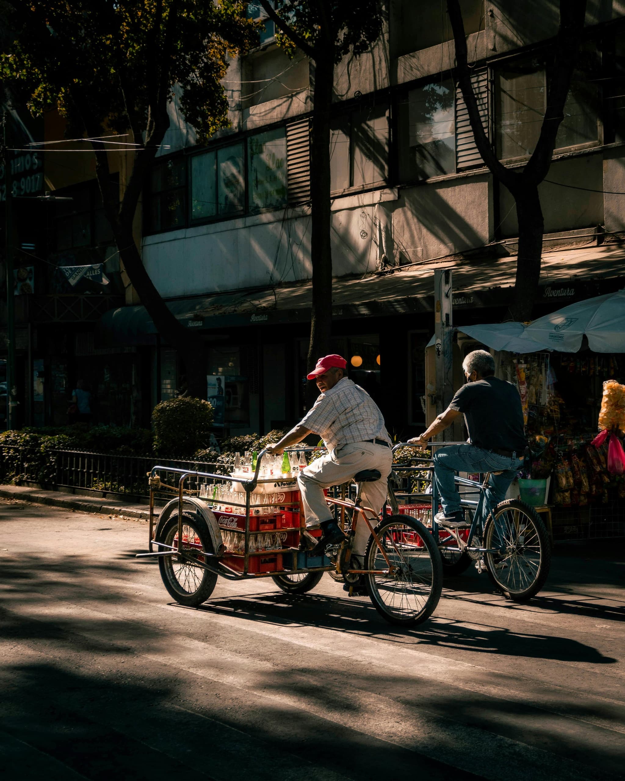 Street vendor tricycle selling snacks on shaded urban avenue
