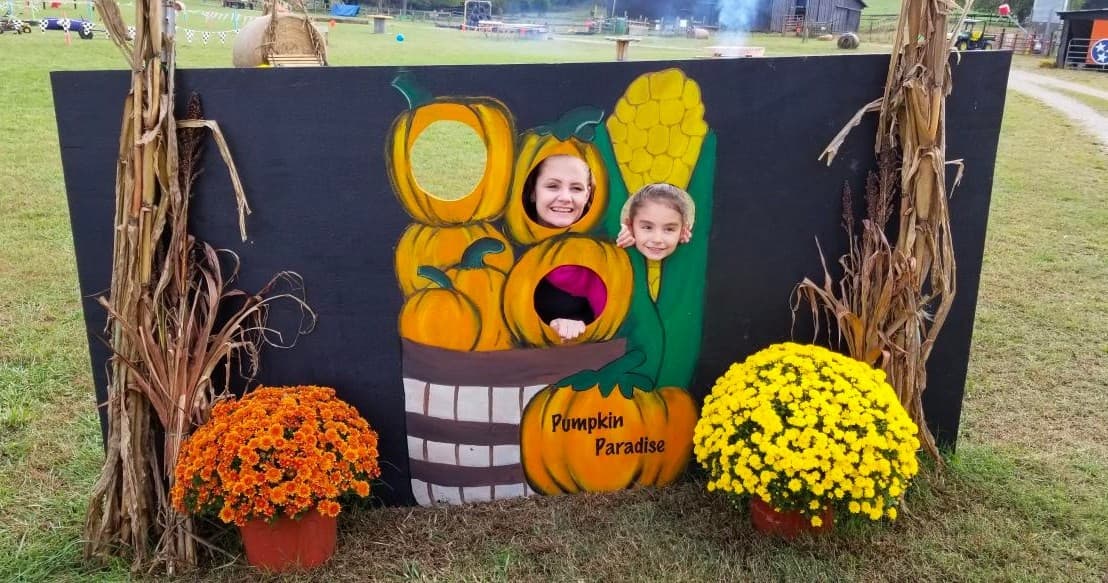 Kids smiling through pumpkin cutout at outdoor patch
