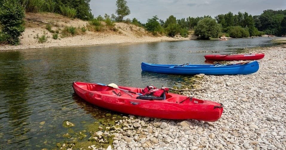 Red and blue kayaks beached on pebble riverbank near trees
