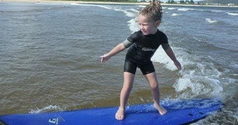 Young child standing on surfboard in gentle Central Coast waves
