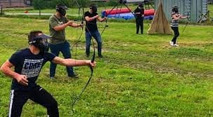 Outdoor archery tag players firing foam arrows across grass field