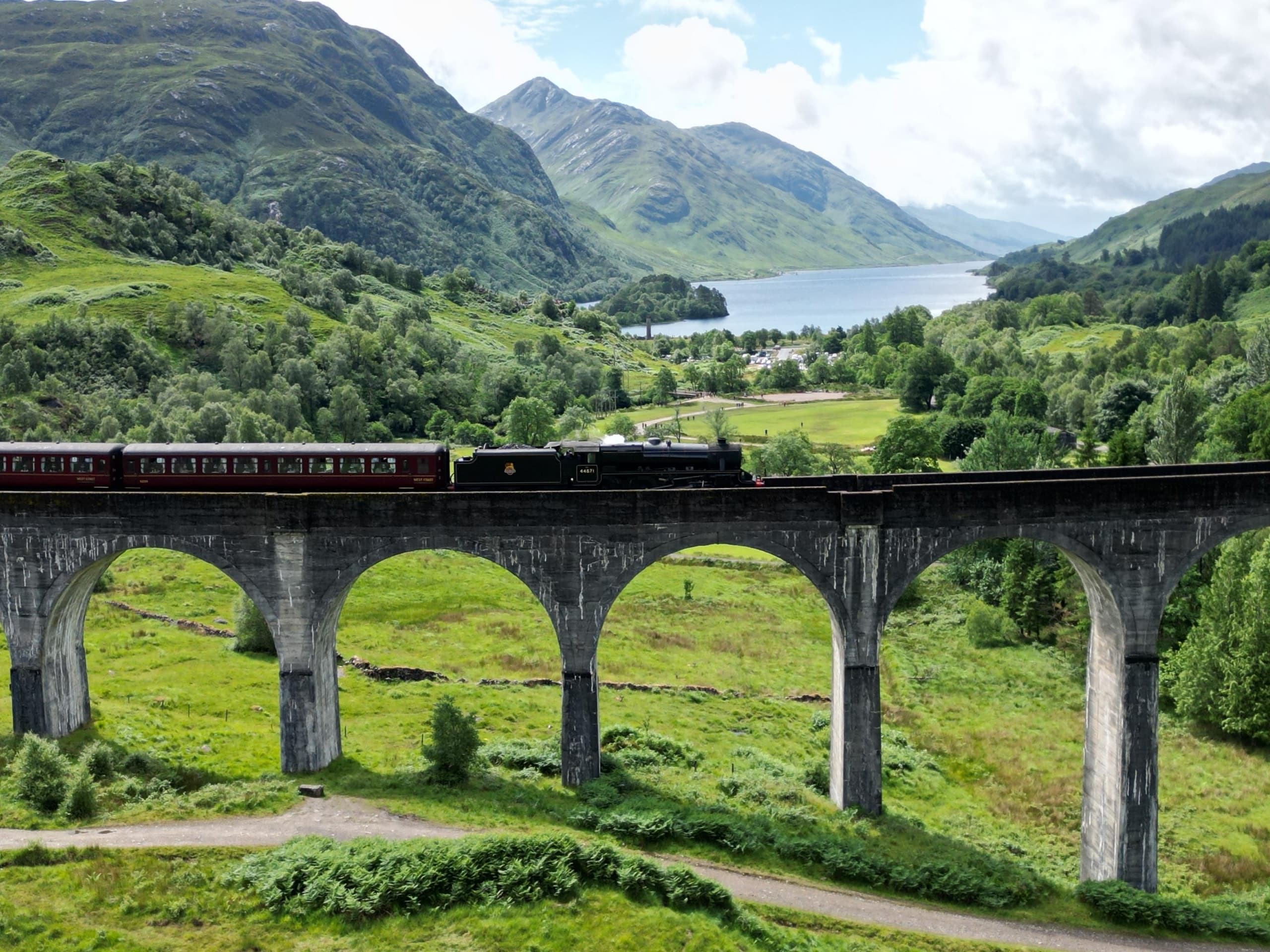 Historic railway viaduct spanning green valley with passing train